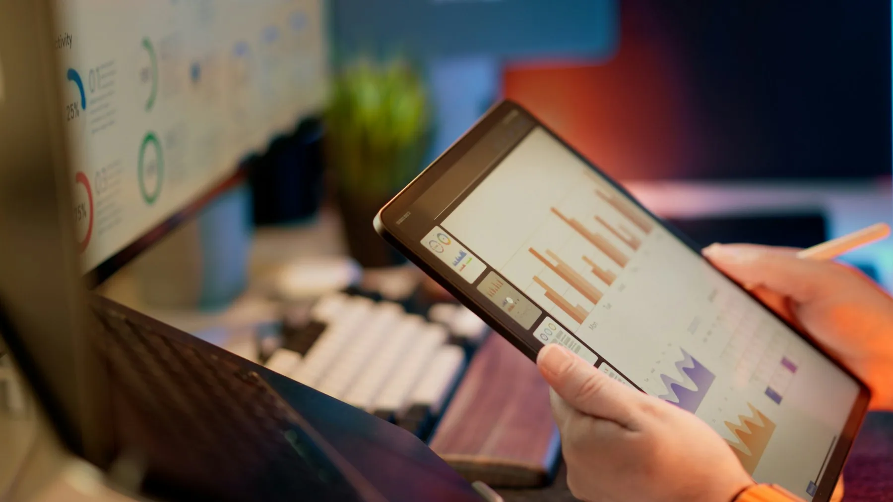 Financial analyst reviewing charts on a tablet beside a desktop dashboard
